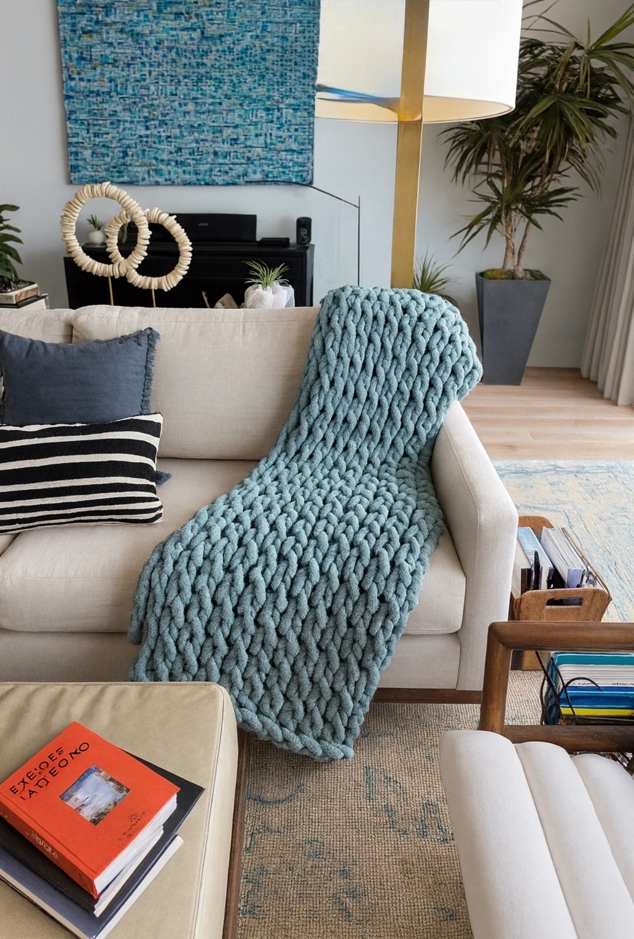 Cozy living room with a beige sofa, blue knitted throw blanket, and decorative items. chunky chenille knit blanket 50x60 styled on neutral sofa styling