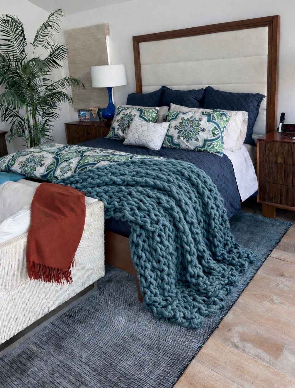 Ocean Blue chunky chenille knit blanket 72x84 styled on neutral sofa styling. Cozy bedroom with a large bed, decorative pillows, and a green throw blanket.