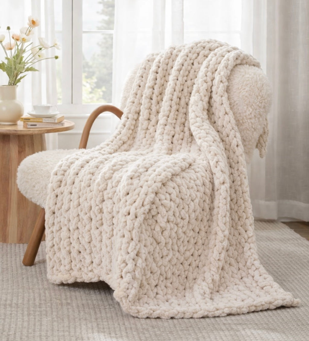 Cozy armchair with a chunky knit beige blanket in a bright room. cream chunky chenille knit blanket 50x60 styled on neutral folded stack
